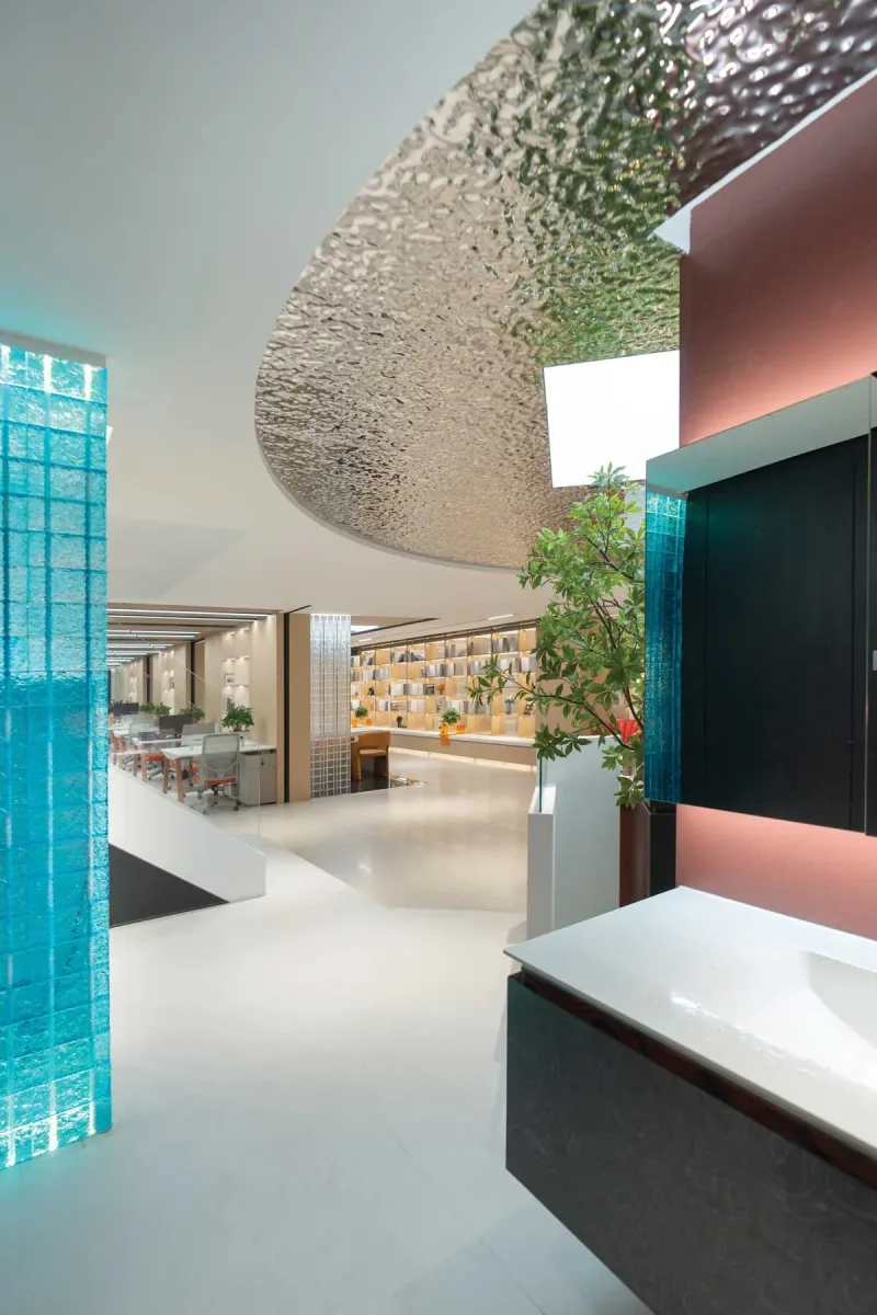 Dettaglio dello showroom Team Value con soffitto metallico ondulato, pareti in vetro azzurro e vista sugli uffici e l’esposizione materiali