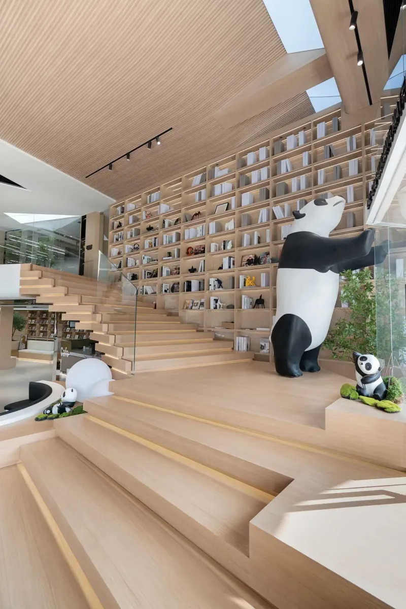 Scalinata in legno nello showroom Team Value con parete-libreria a tutta altezza e grandi figure di panda che arricchiscono lo spazio espositivo