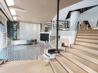 Vista d’ingresso dello showroom Team Value con scala in legno, camino sospeso e pavimento decorativo in bianco e nero