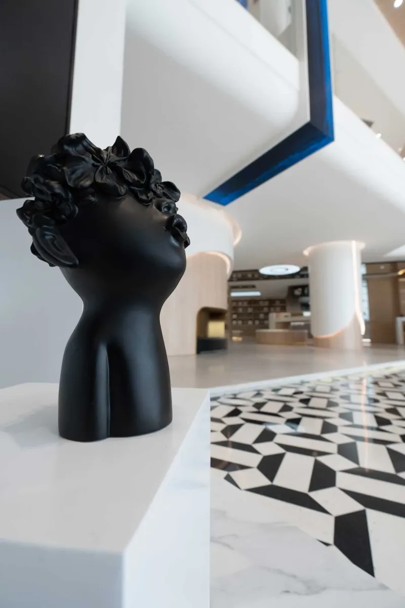 Scultura nera su piedistallo nello showroom Team Value, con pavimento geometrico in bianco e nero e dettagli architettonici curvi sullo sfondo
