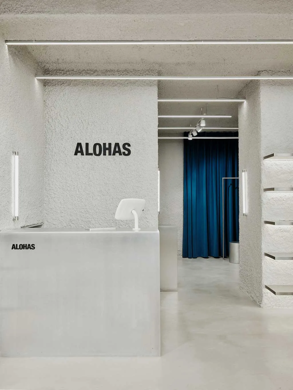 Dettaglio del banco cassa e delle superfici materiche del flagship store ALOHAS a Madrid, con tenda blu a contrasto progettata da Clap Studio