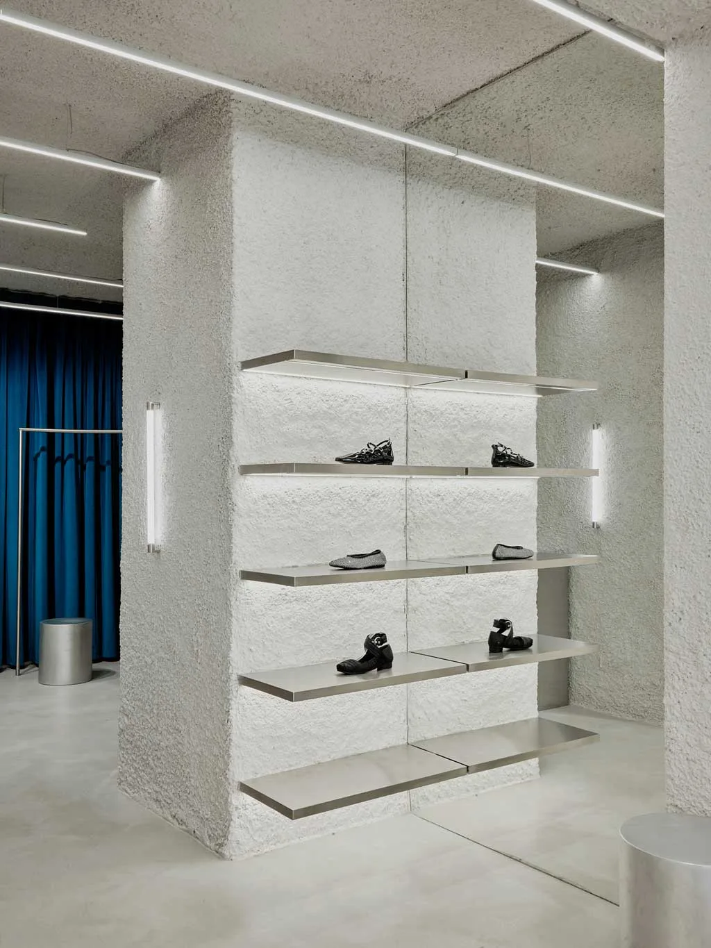 Mensole sospese in metallo e pareti materiche nel flagship store ALOHAS a Madrid, con giochi di riflessi e superfici specchiate ideate da Clap Studio