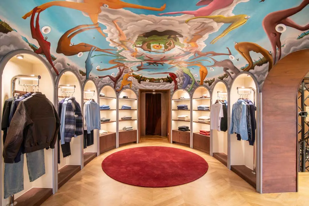 Sala “Eyes Wide Shut” del flagship store Nude Project con affresco surrealista di Pedro Hoz e nicchie espositive ad arco illuminate