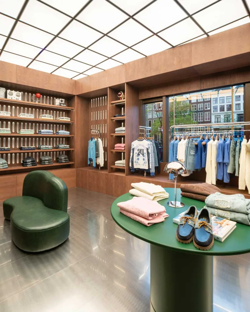 Sala “2001: Odissea nello Spazio” del flagship store Nude Project con arredi in legno, divano verde e soffitto luminoso geometrico