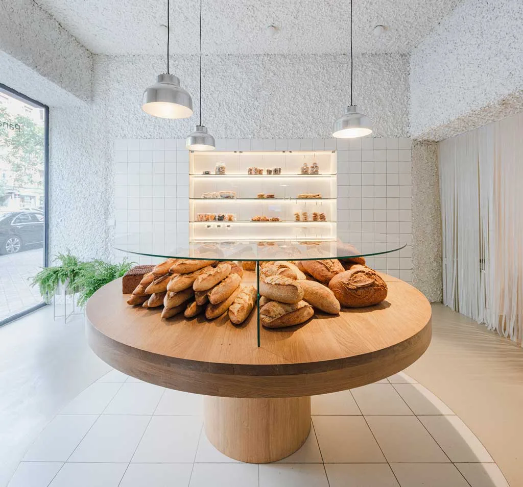 Round wooden table with displayed bread at Babette Bakery on Paseo de la Habana, an example of interior design for bakeries by ZOOCO ESTUDIO.