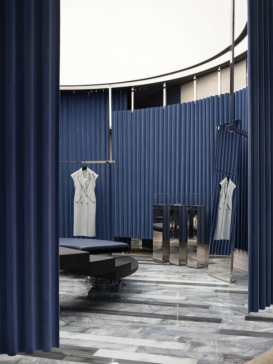Vista interna della boutique MITHRIDATE a Guangzhou con pavimento in marmo e tende blu ondulate – un esempio di retail design esperienziale di SLT Design