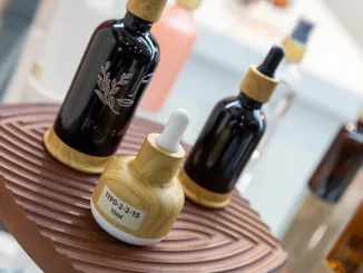 Flaconi cosmetici in vetro scuro con tappo effetto legno esposti a Packaging Première & PCD Milan 2025 su supporto in legno scolpito