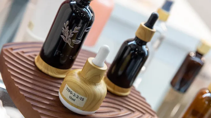 Flaconi cosmetici in vetro scuro con tappo effetto legno esposti a Packaging Première & PCD Milan 2025 su supporto in legno scolpito