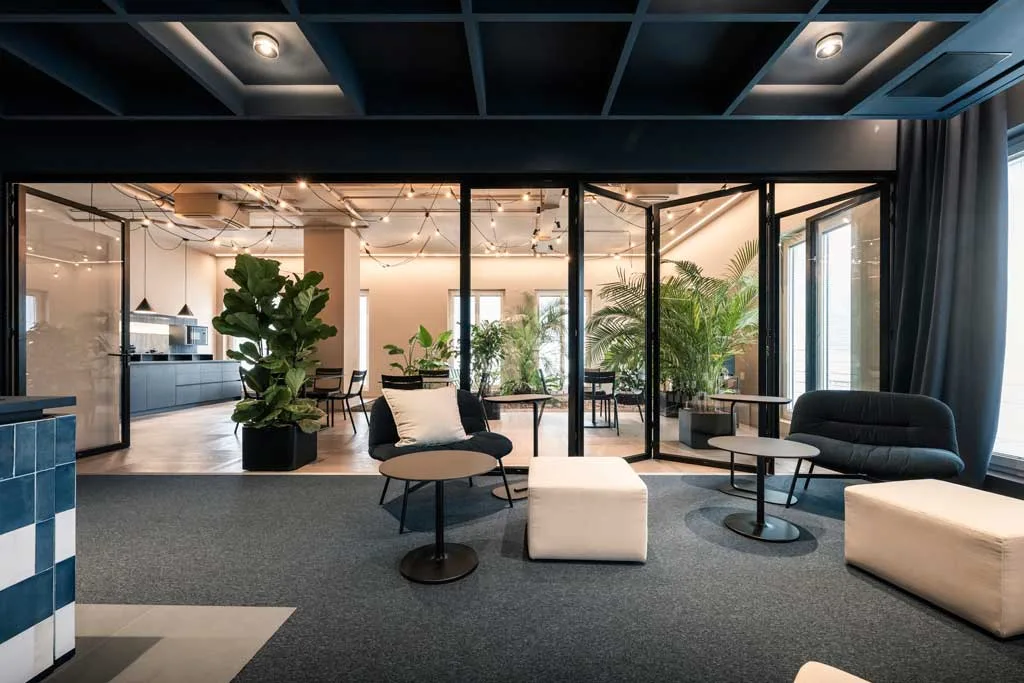 Zona lounge con vista sulla cucina e sala riunioni immerse nel verde, all’interno della sede ADDITIVE a Bolzano progettata da NOA