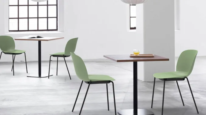 Sedie Plose di Segis in polipropilene verde con struttura in metallo nero, ambientate in uno spazio minimal contemporaneo con tavoli quadrati e luce naturale
