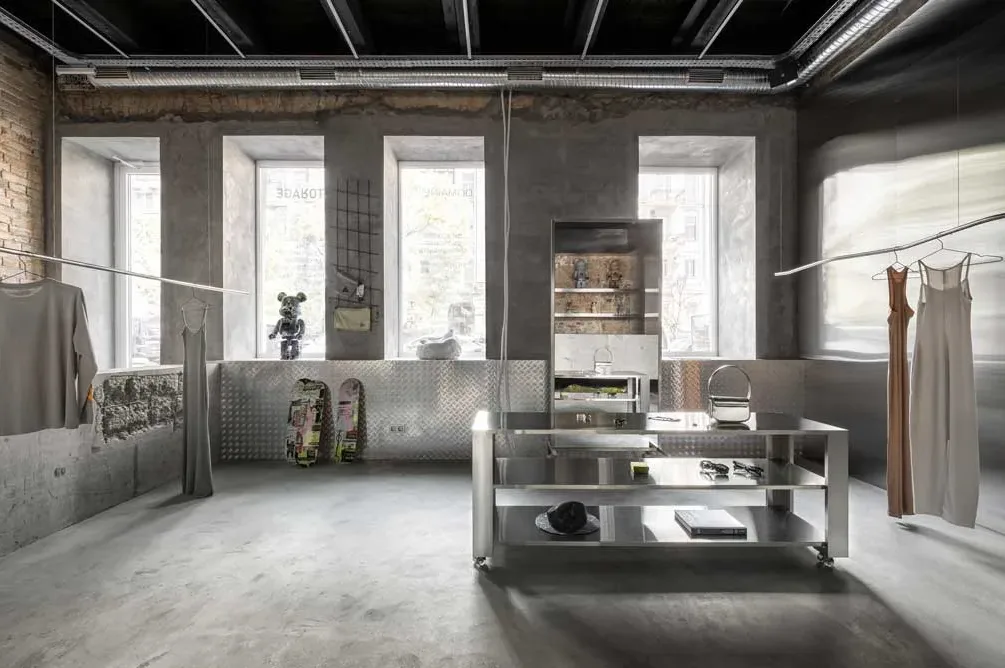 Vista frontale dello showroom Domaine 17 a Kiev, con esposizione di capi minimalisti, arredi in acciaio lucido e dettagli urbani come skateboard decorativi.