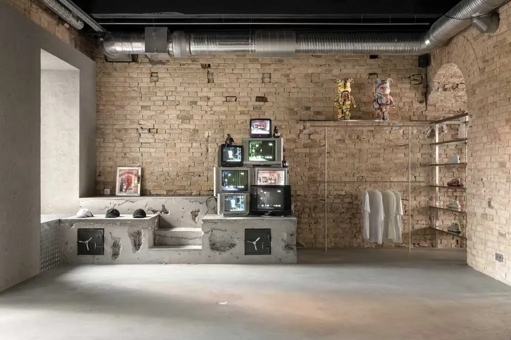 Installazione artistica con vecchi televisori nello showroom Storage x Domaine 17 a Kiev, su sfondo di mattoni originali e arredi industriali in cemento.