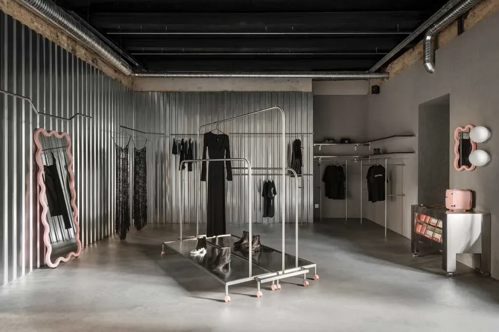 Showroom Domaine 17 a Kiev con pareti in acciaio ondulato, specchi rosa ondulati e stender metallici su ruote.