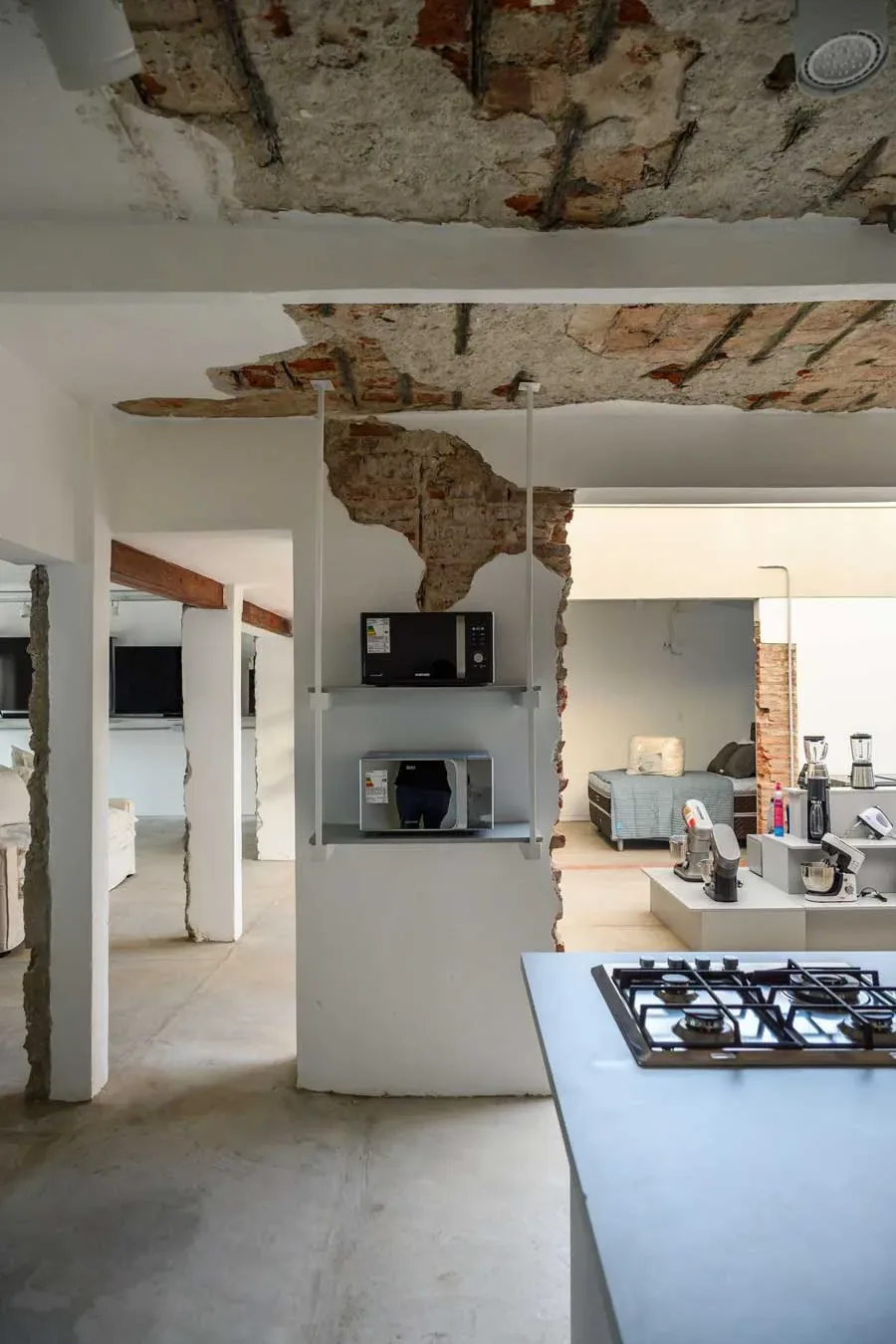 Elementi strutturali originali e segni del tempo a soffitto e pareti nel progetto Natalia Hogar, con esposizione di piccoli elettrodomestici integrata