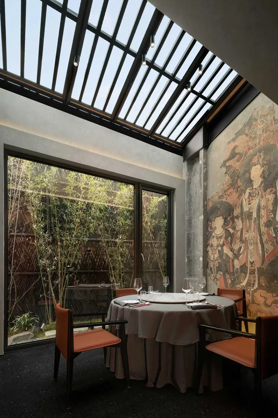 Tavolo rotondo del ristorante GUI TEMPLE a Pechino con affresco ispirato al Tempio Fahai e vista su giardino di bambù