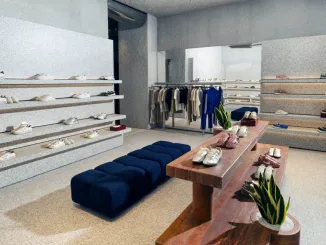Interni della boutique Autry in Rue Saint-Honoré a Parigi con tavolo in travertino rosso e seduta blu, tra design materico e sneakers esposte