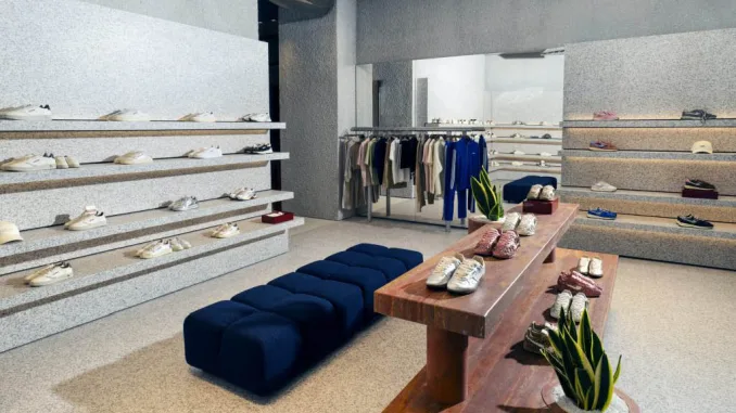 Interni della boutique Autry in Rue Saint-Honoré a Parigi con tavolo in travertino rosso e seduta blu, tra design materico e sneakers esposte