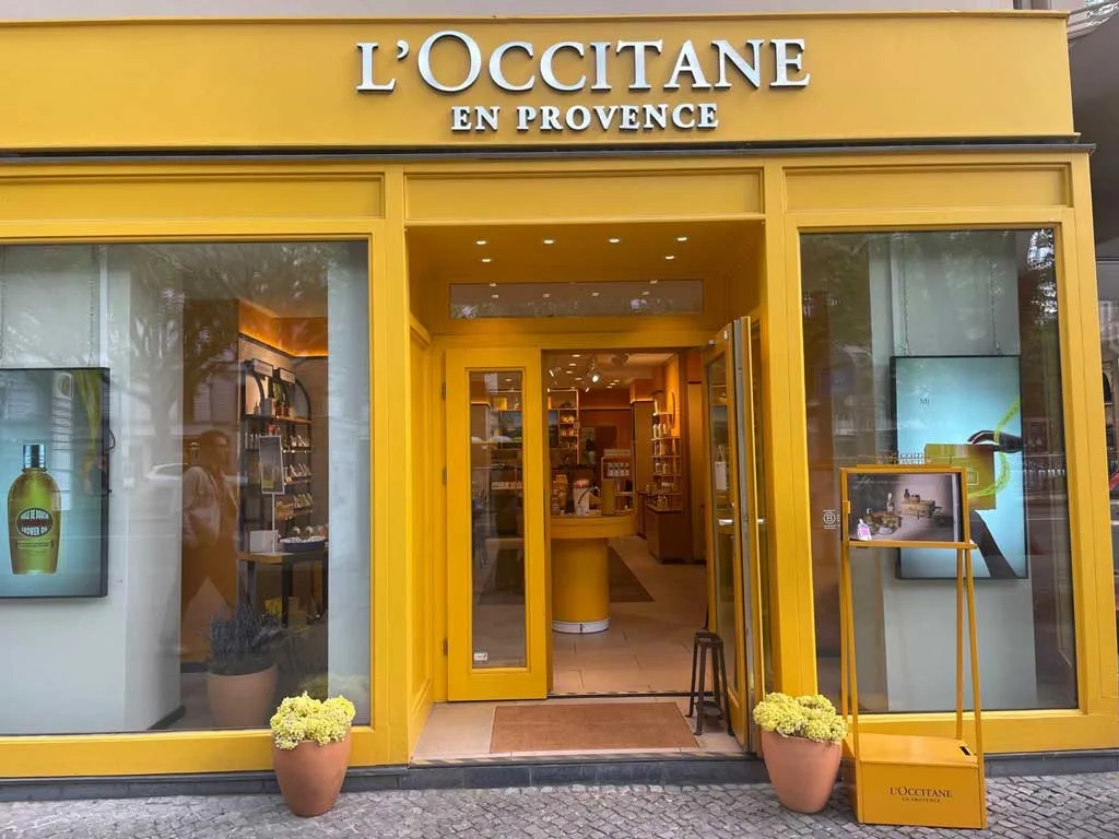 Entrance of L’Occitane en Provence store in Berlin with yellow façade and floral displays