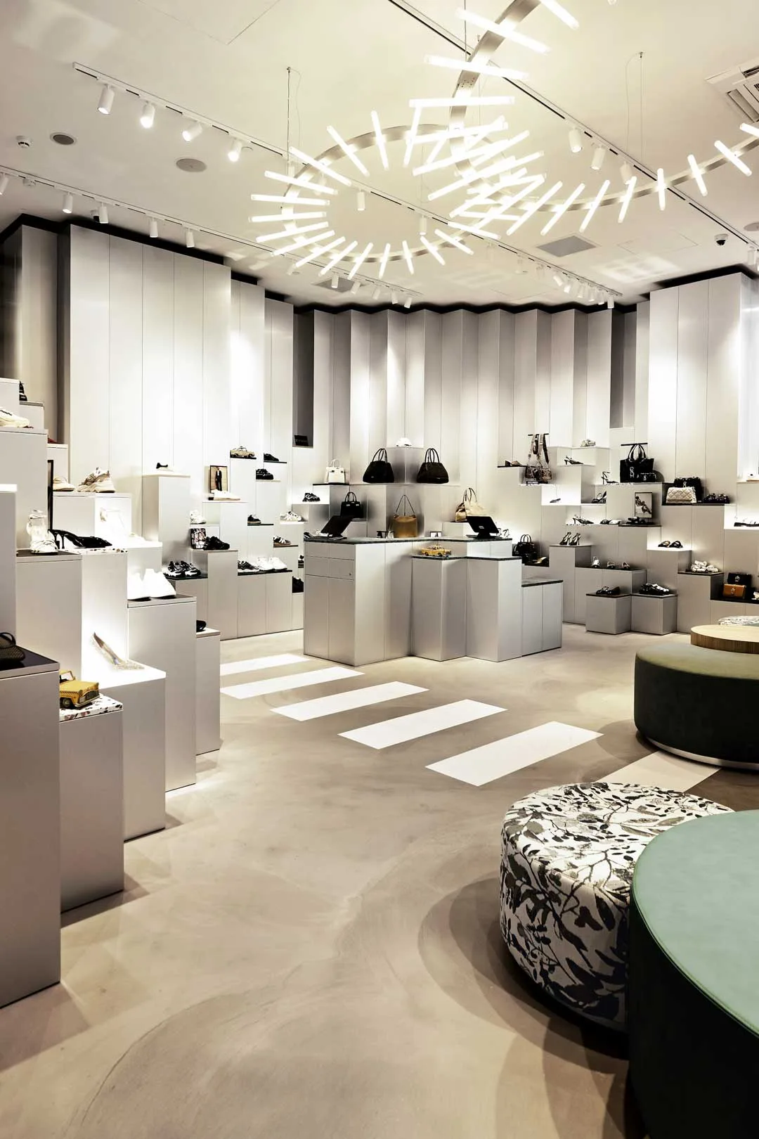 Esposizione interna del concept store Steve Madden nei Paesi Bassi con pareti retroilluminate, pedane modulari per calzature e borse, sedute imbottite e installazione luminosa circolare a soffitto.