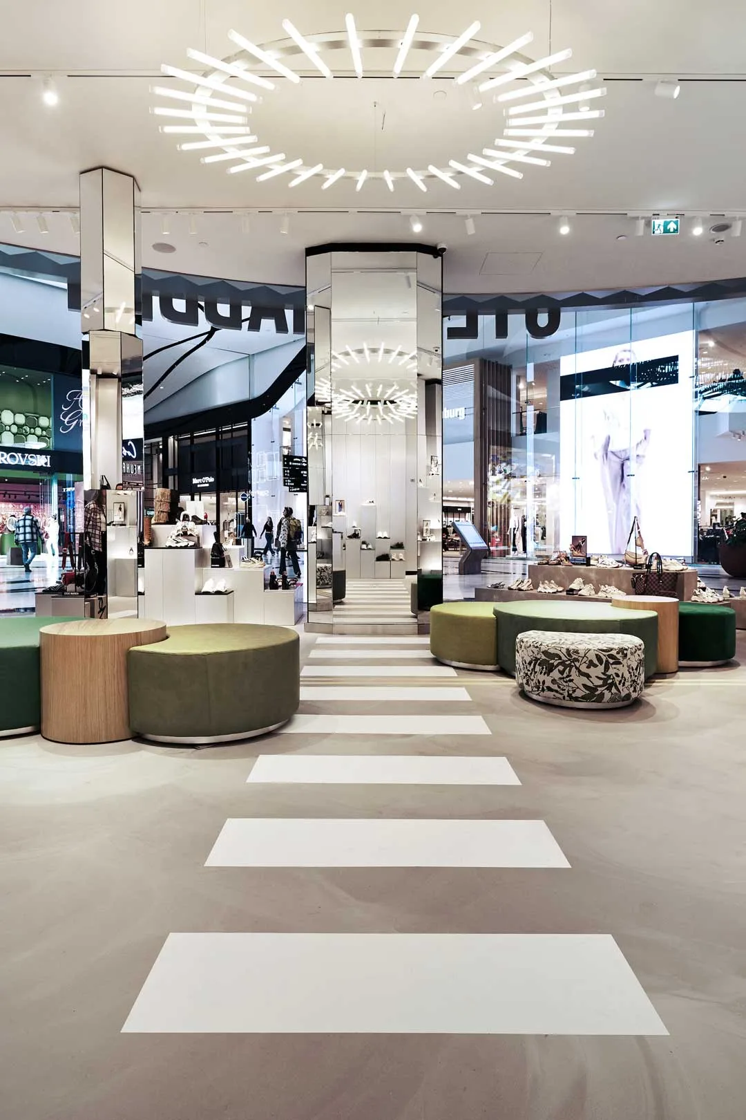 Vista interna del concept store Steve Madden nei Paesi Bassi con sedute circolari, pilastri specchiati, illuminazione scultorea e display espositivi in un ambiente retail contemporaneo.