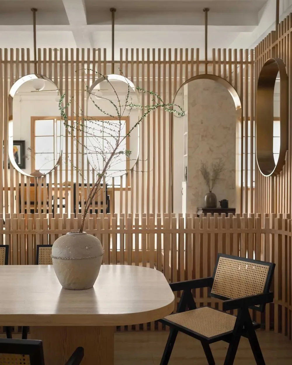 Dettaglio della sala da tè nella teahouse artistica a Foshan, con tavolo in legno chiaro, sedute in paglia di Vienna e pareti divisorie con specchi ovali dorati