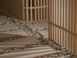 Dettaglio del percorso zen nella teahouse artistica a Foshan, con pavimentazione in legno su letto di ciottoli e pareti in listelli verticali firmate Lim + Lu