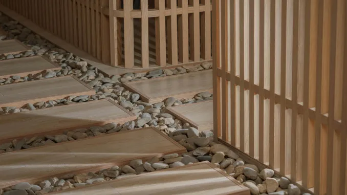 Dettaglio del percorso zen nella teahouse artistica a Foshan, con pavimentazione in legno su letto di ciottoli e pareti in listelli verticali firmate Lim + Lu