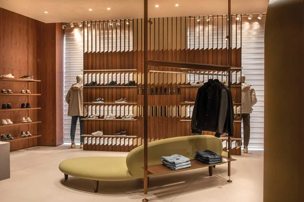 Dettaglio interno della boutique Caposerio Uomo a Cefalù con arredi in noce americano, frangiluce bronzati e area espositiva per calzature e abbigliamento.