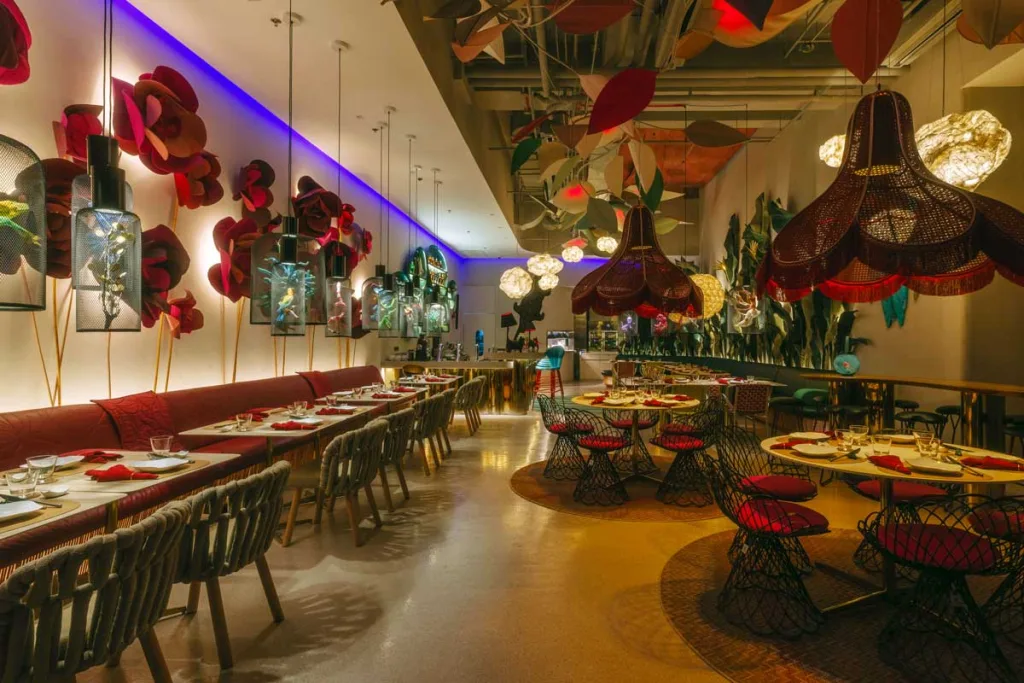 Dettaglio degli interni del FABLE Café + Lounge a Manila con fiori giganti alle pareti, lampade scenografiche e tavoli rotondi in stile tropicale-artigianale