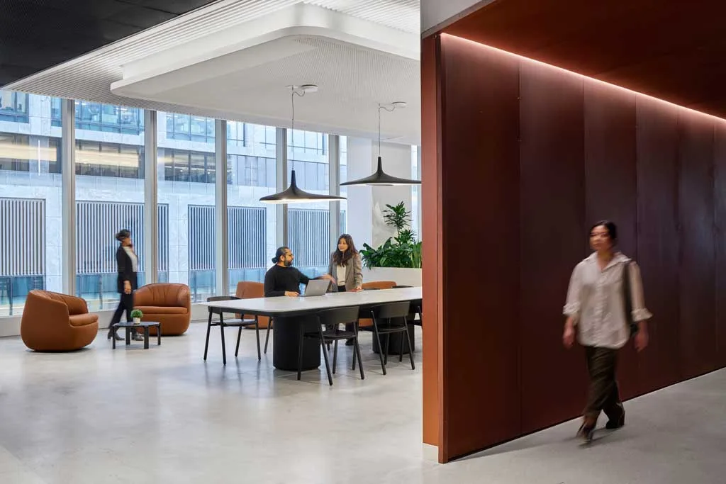 Spazio di coworking con tavolo condiviso, poltrone in pelle color cuoio e ampie vetrate panoramiche presso l'HSBC Zero Carbon HQ sostenibile.