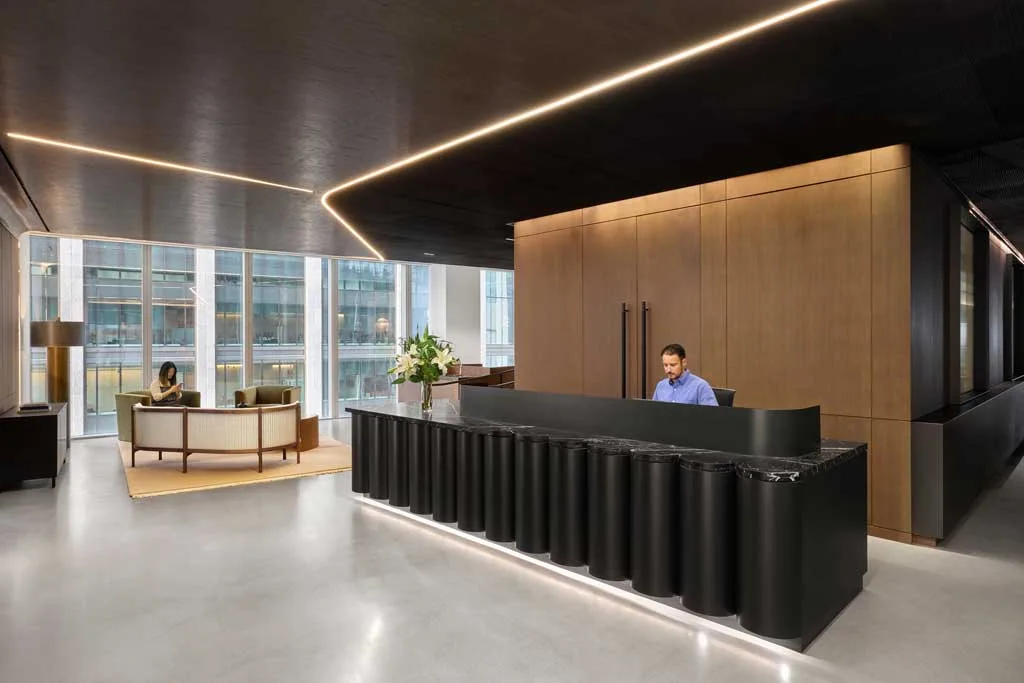 Reception dal design elegante con bancone nero in marmo e legno, illuminazione a LED integrata e area lounge con poltrone presso l'HSBC Zero Carbon HQ sostenibile.