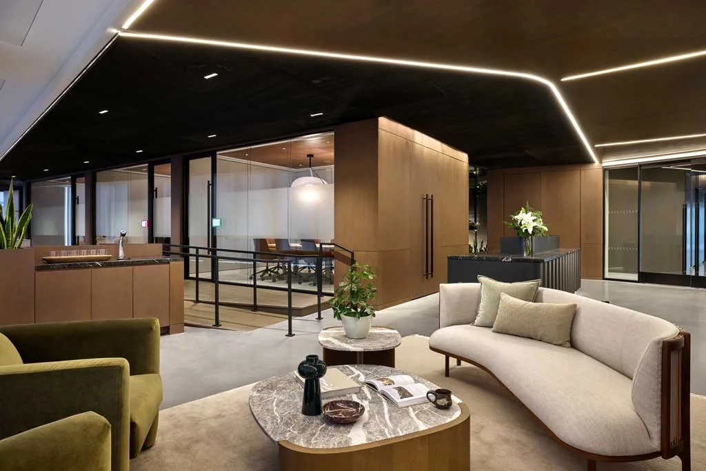 Lounge adiacente alle sale riunioni con divano curvo, poltrona verde, tavolini in marmo e arredi in legno presso l'HSBC Zero Carbon HQ sostenibile.