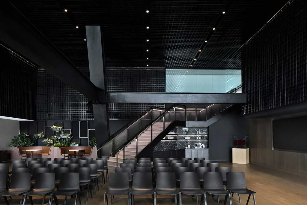 Sala conferenze con sedute nere, scala industriale in metallo e design contemporaneo con pareti e soffitto a griglia presso l'HSBC Zero Carbon HQ sostenibile.