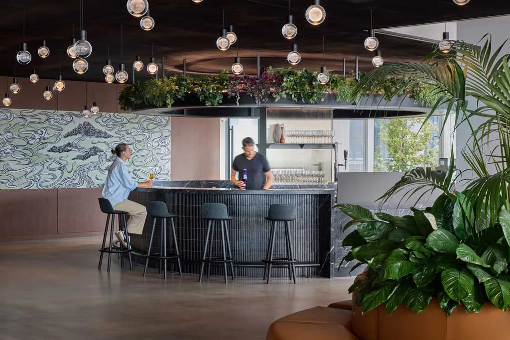Area bar dal design contemporaneo con lampade a globo sospese, piante decorative e bancone in nero, all'interno dell'HSBC Zero Carbon HQ sostenibile