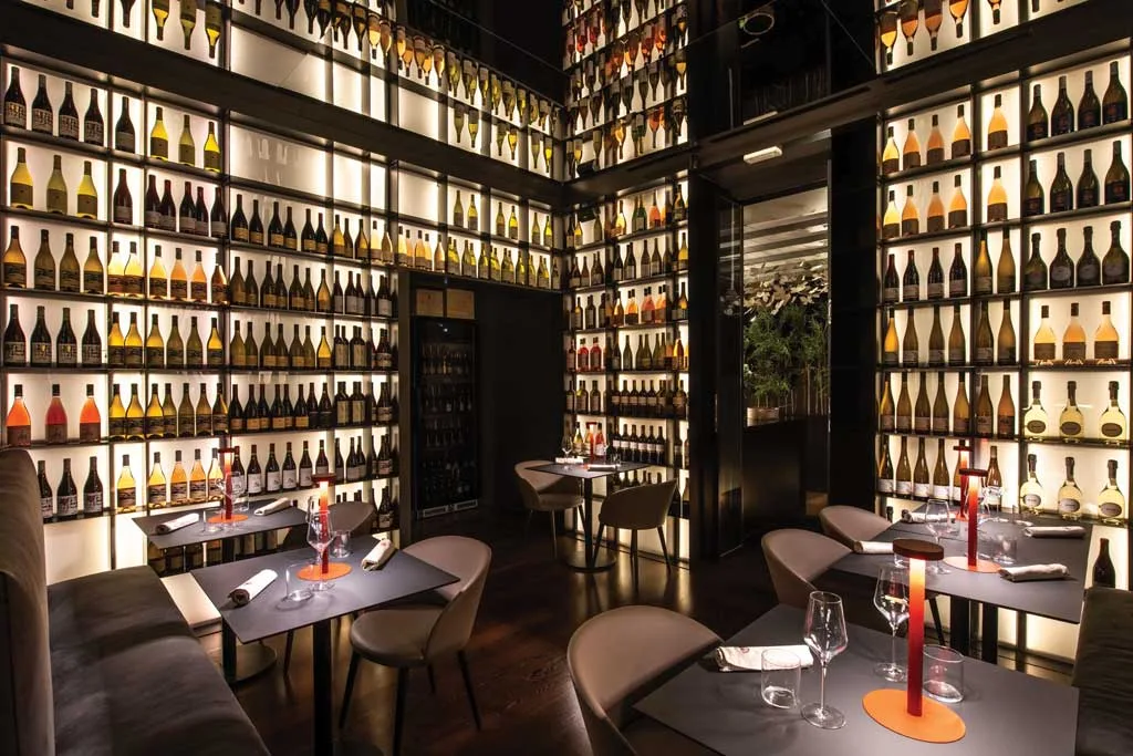 Scenographic wine wall at HIO Sushi Lab in Palermo, backlit full-height bottle display with set dining tables.
