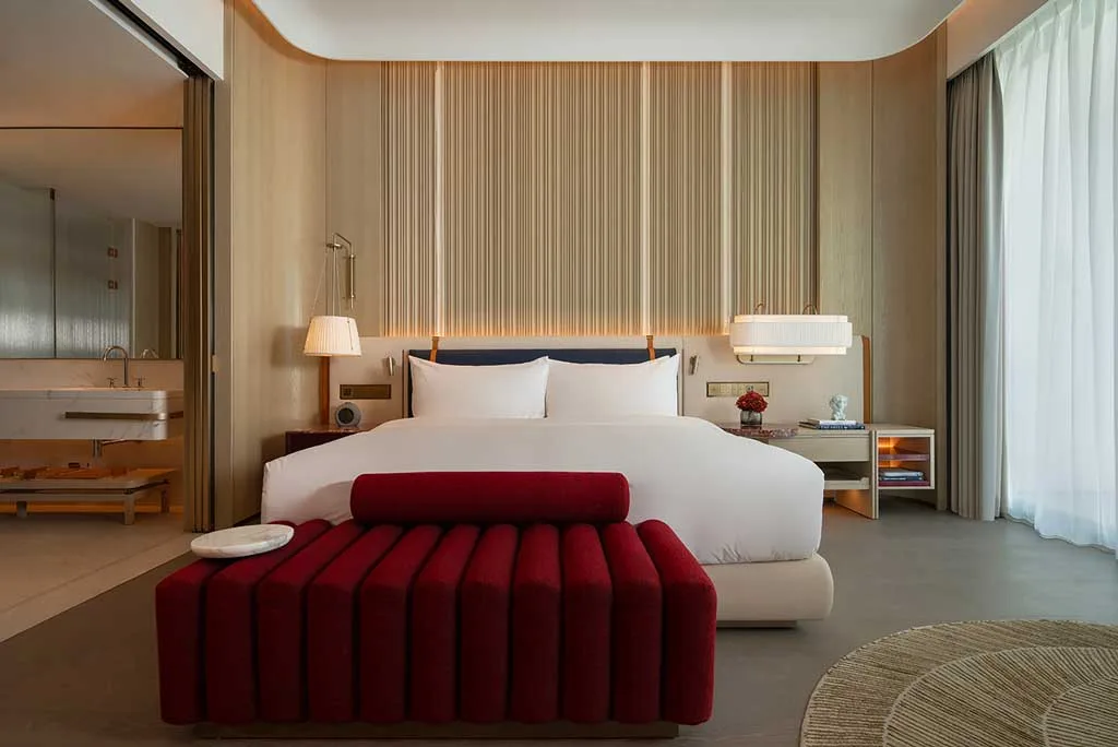 Camera del MGM Shenzhen progettato da CCD, con letto matrimoniale, dettagli in legno, panca imbottita rossa e vista luminosa verso l’esterno.