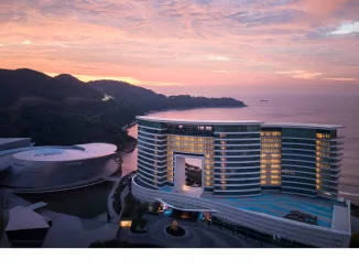 Vista esterna del MGM Shenzhen progettato da CCD, hotel di lusso fronte mare con architettura trapezoidale e facciata vetrata al tramonto