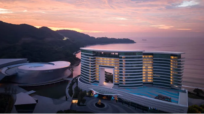 Vista esterna del MGM Shenzhen progettato da CCD, hotel di lusso fronte mare con architettura trapezoidale e facciata vetrata al tramonto