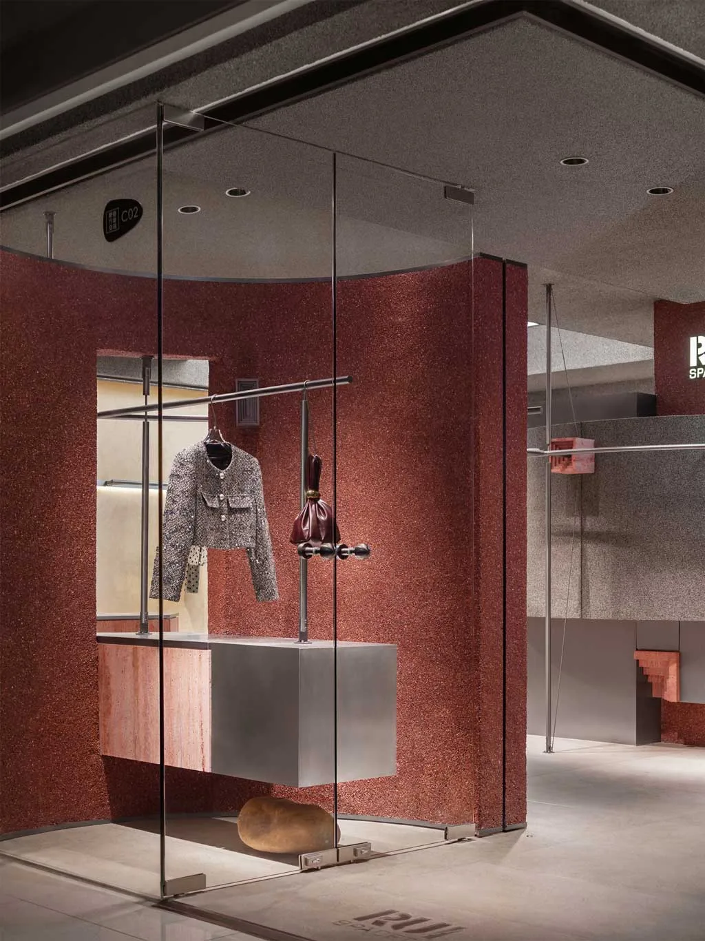 Dettaglio interno del concept store RUI SPACETIME con pareti in pietra resinata grigia e logo retroilluminato