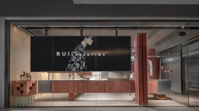 Vista esterna del RUI SPACETIME Concept Store a Shenzhen con facciata in vetro, rivestimenti in travertino rosso e installazione multimediale