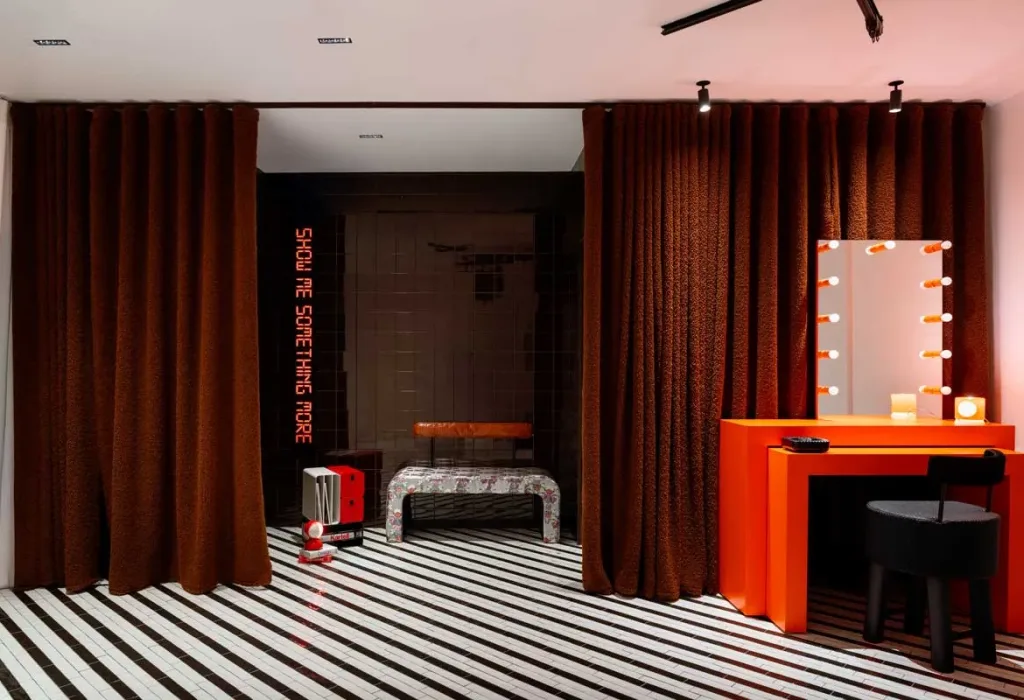 Spogliatoio e zona trucco di Boom Town Projects con tenda marrone e vanity table arancione disegnati da Carmine Abate