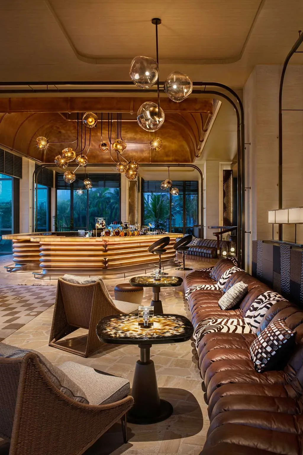 Bar del Kimpton Aqeos Hainan con soffitto in rame, illuminazione calda e arredi dal design curvilineo.