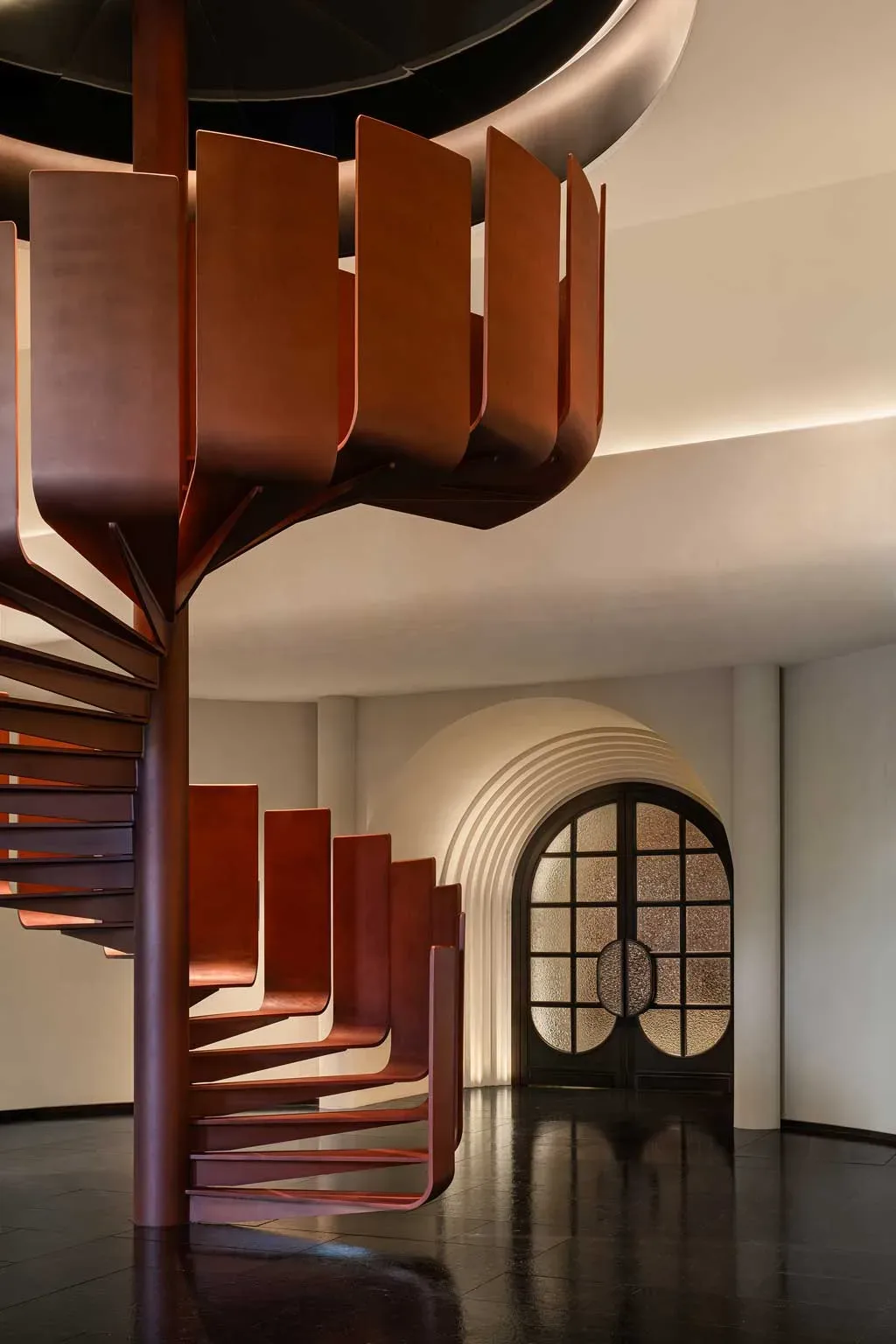 Scalinata a chiocciola in metallo brunito nel Kimpton Aqeos Hainan, con design scultoreo e finiture eleganti.