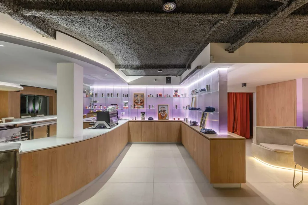 Bancone principale del bar Ciudadano a Córdoba, con finiture in legno chiaro, pareti retroilluminate e scaffalature espositive integrate.