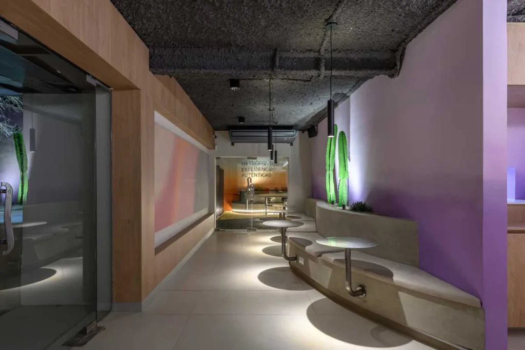 Sedute integrate e tavolini curvi nell’interno del bar Ciudadano a Córdoba, con pareti sfumate e illuminazione d’accento.