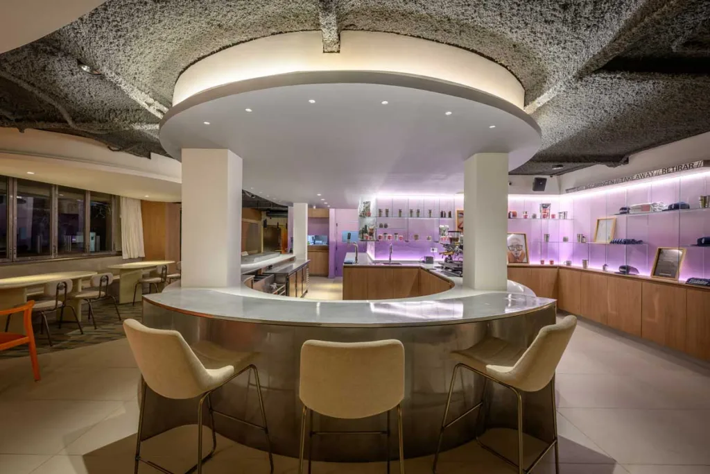 Vista del bancone curvo del bar Ciudadano a Córdoba, con sedute alte, finiture metalliche e illuminazione soffusa che valorizza il design fluido dello spazio.