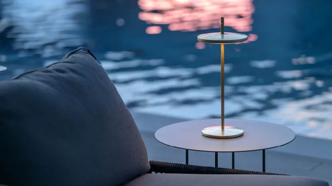 Lampada Thaïs di Platek in ottone con finitura stone washed posata su tavolino outdoor vicino a una piscina al tramonto