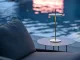 Lampada Thaïs di Platek in ottone con finitura stone washed posata su tavolino outdoor vicino a una piscina al tramonto
