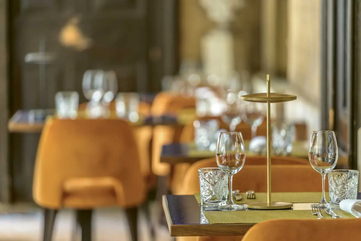 Lampada Thaïs di Platek in ottone collocata su tavolo apparecchiato in ambiente ristorante con sedute color ocra