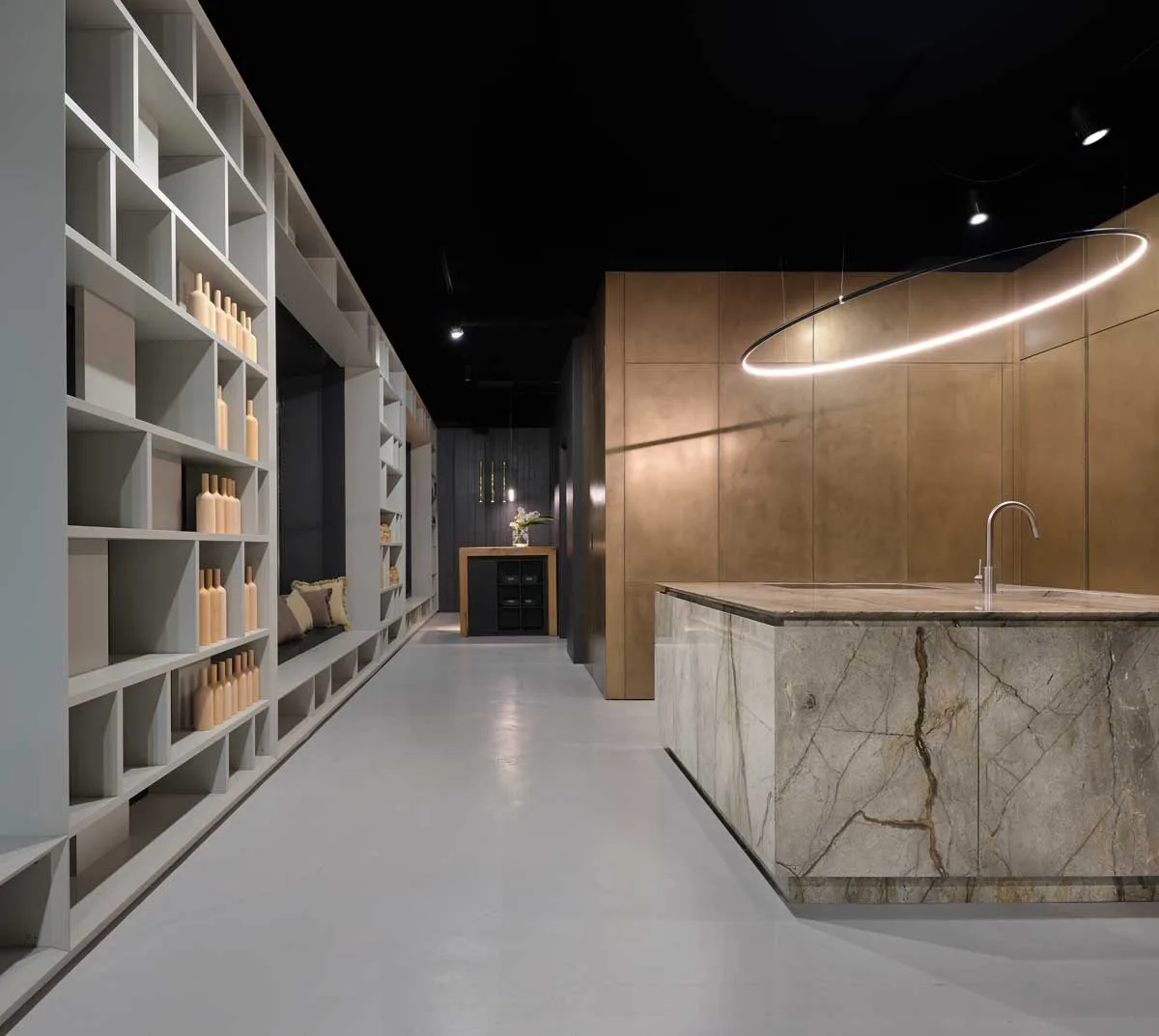 Showroom RiFRA Milano con isola in pietra naturale, libreria a parete e pannelli metallici bronzati
